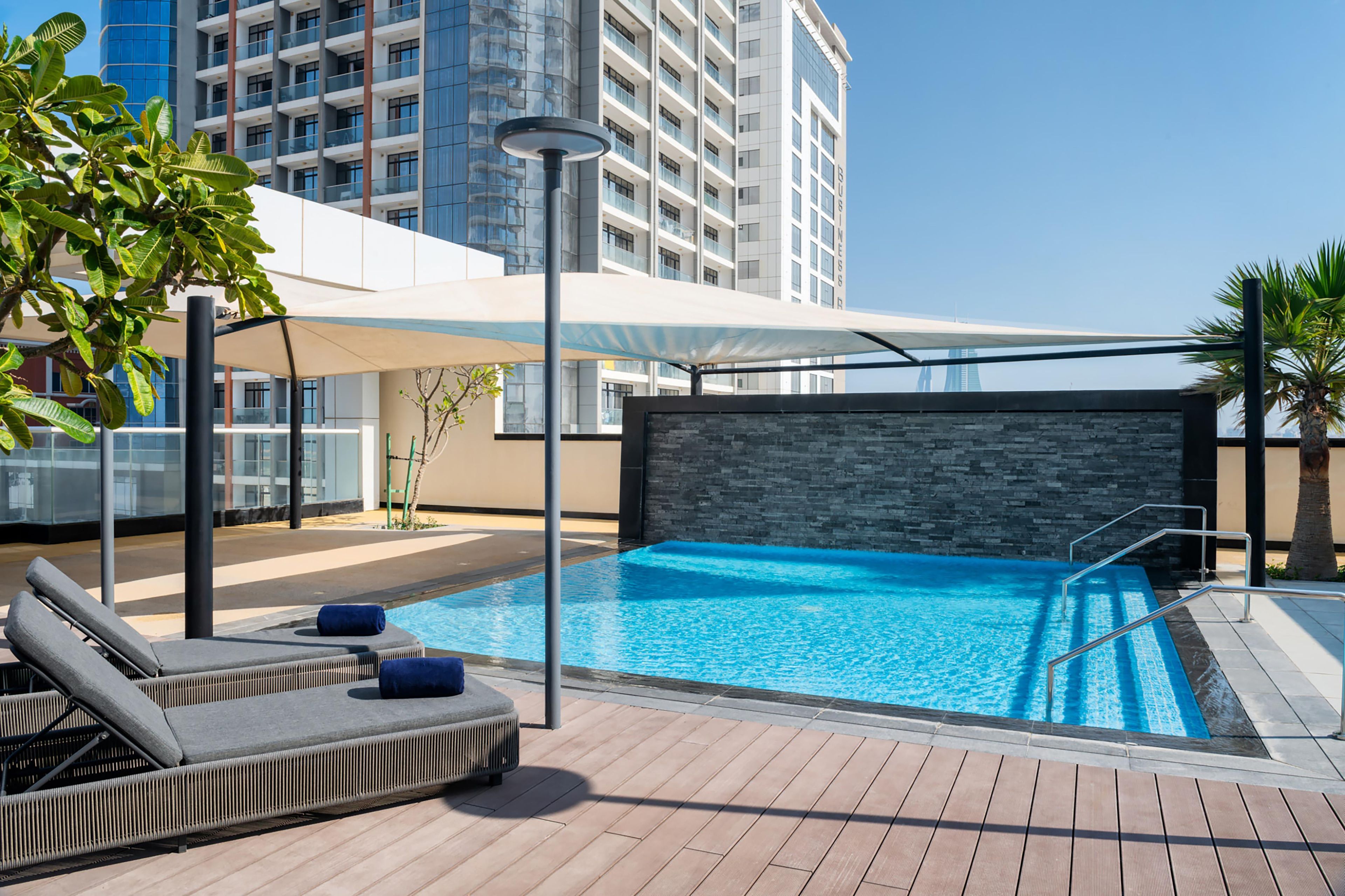 A rooftop pool with lounge chairs and a view of a high-rise building.