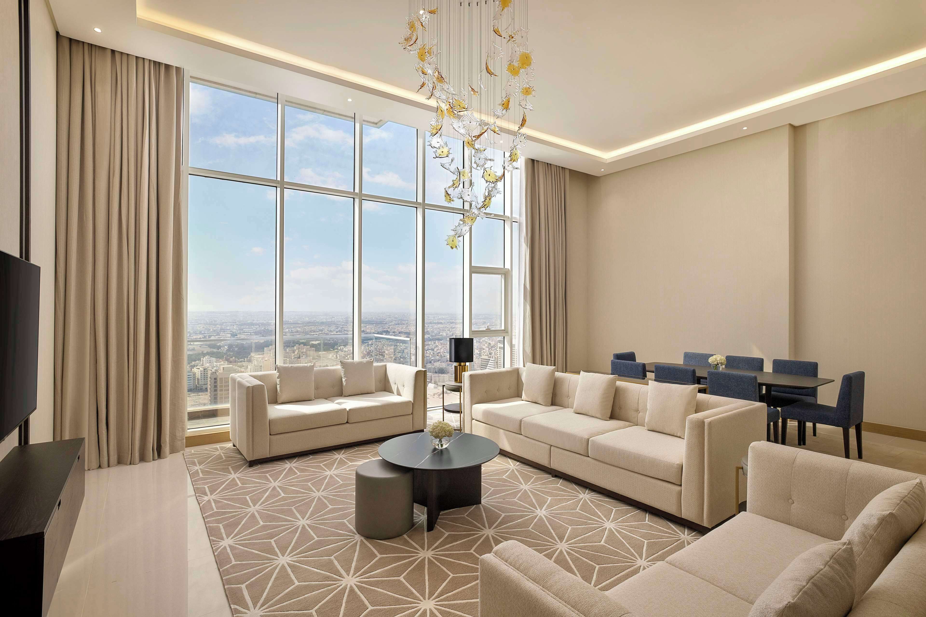 A spacious living room with a large window, a chandelier, and a city view.