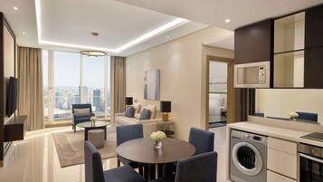 A modern hotel room with a large window, a round dining table, a sofa, a washing machine, and a microwave.