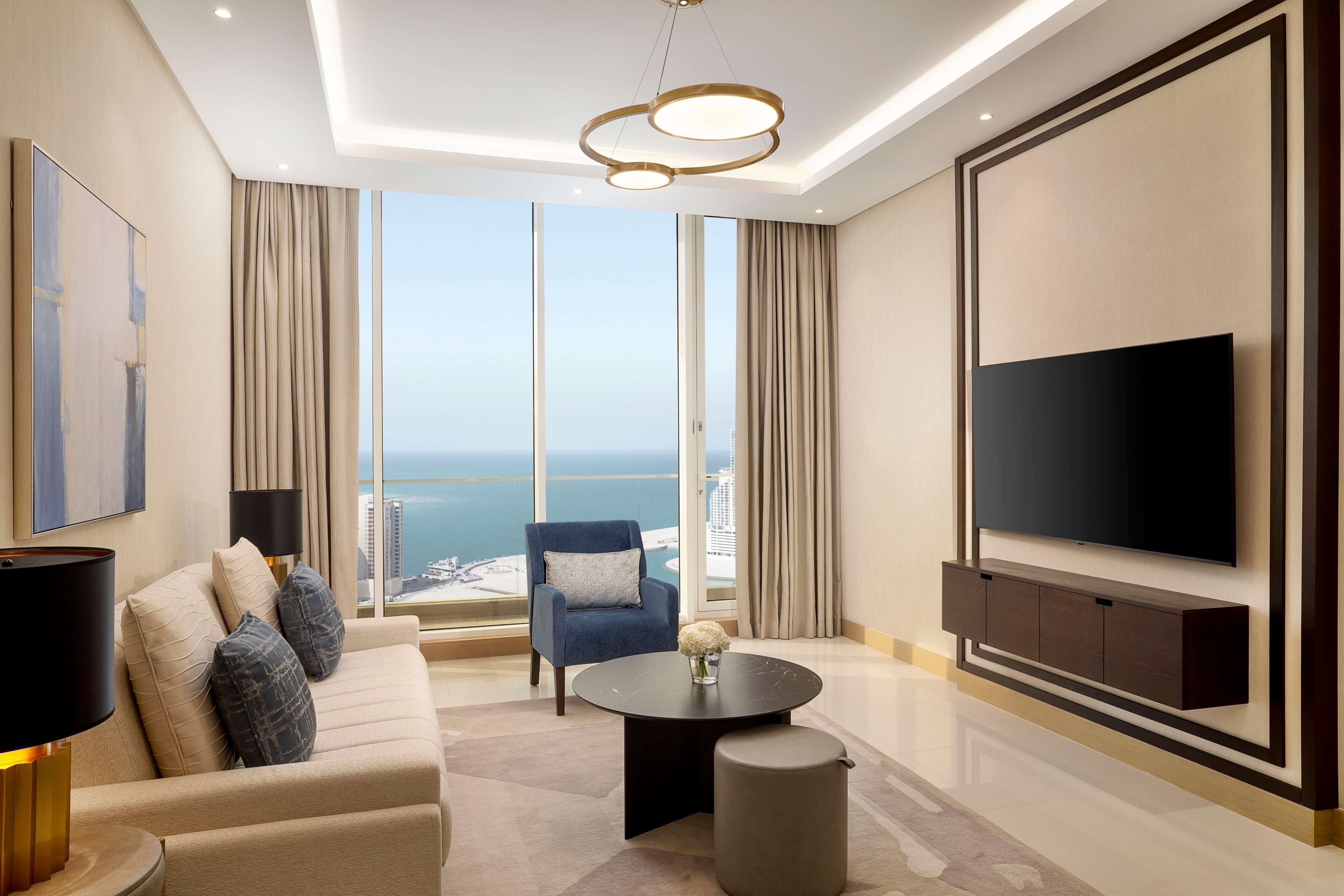 Un salon moderne doté d’un grand téléviseur à écran plat, d’un canapé, d’une table basse et offrant une vue sur la ville et la mer grâce à de grandes fenêtres.