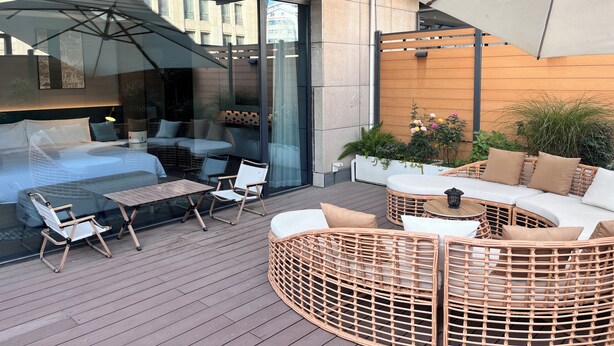 A modern outdoor seating area with wicker furniture, a glass partition, and a wooden wall. - Hilton Garden Inn Xi'An Bell Tower (Xi'an)