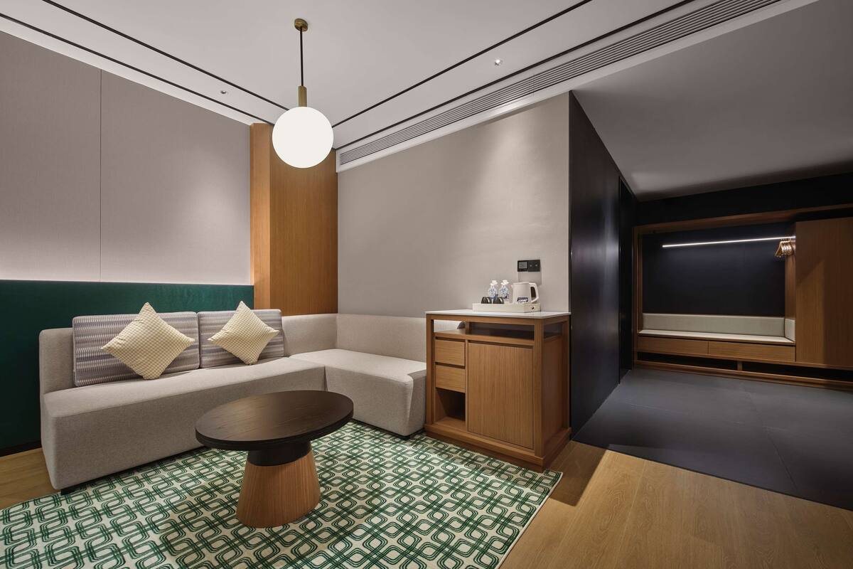 A modern hotel room with a sofa, a coffee table, a desk, and a mirror.