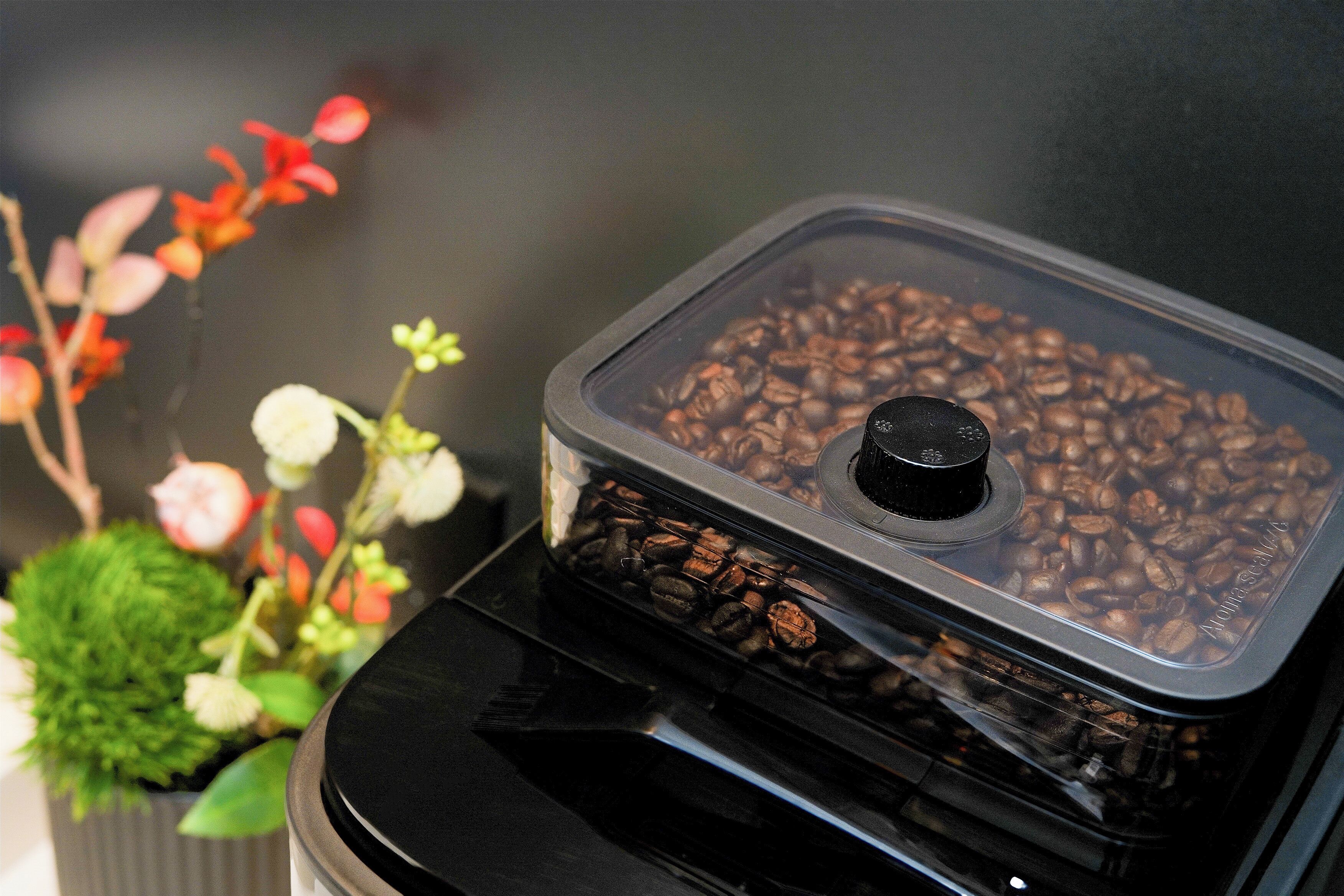 Una cafetera con un recipiente transparente lleno de granos de café.