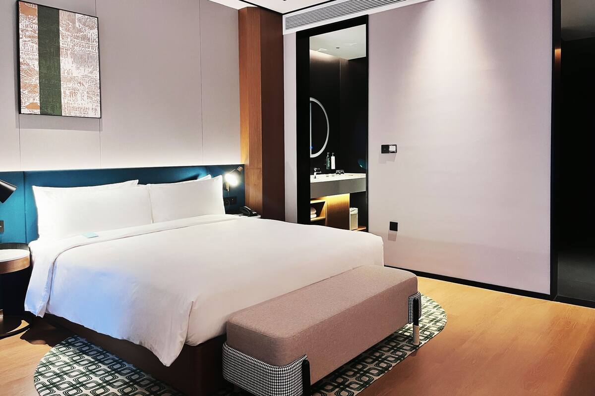 A modern hotel room with a large bed, a bedside table, a mirror, and a bathroom visible through an open door.