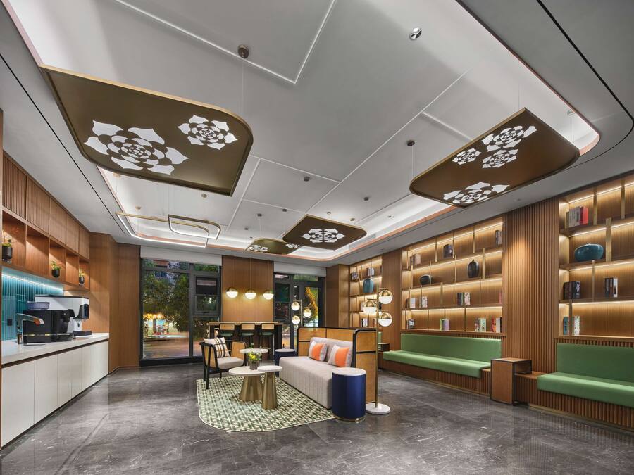 A modern hotel lobby with a reception desk, seating areas, and a bookshelf.
