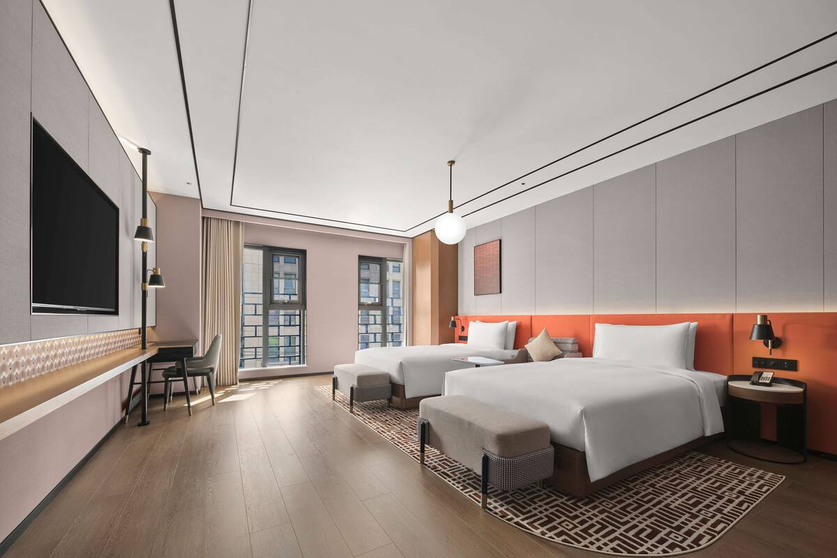 A modern hotel room with two beds, a desk, and a large TV.