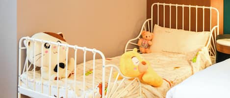 A child's bed with a white metal frame, a plush toy, and a pillow.