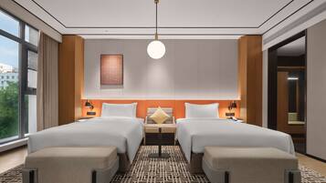 Een moderne hotelkamer met twee bedden, een groot raam, een kamerbreed tapijt met dessin en een wandlamp.