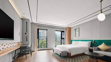 Una habitación de hotel moderna con una cama grande, un escritorio, una silla y un sofá. Un ventanal grande ofrece vistas de edificios.