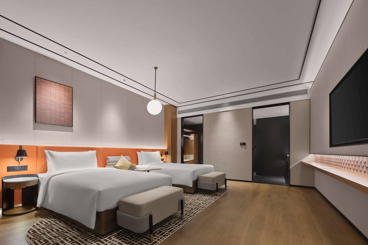 A modern hotel room with two beds, a large window, and a flat-screen TV.
