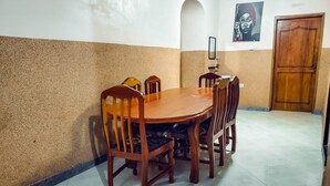 A dining area with a round wooden table and six chairs, a wooden door, and a wall with a textured finish and a framed artwork. - Charming 3-bedroom apartment in wonderful Zanzibar with AC, WiFi (Zanzibar)