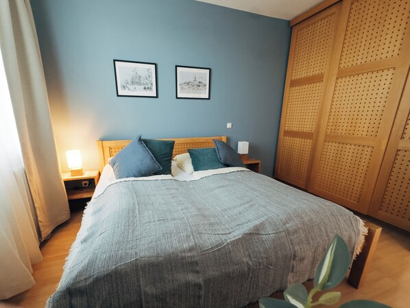 A bedroom with a bed, two framed pictures on the wall, a nightstand with a lamp, and a wooden wardrobe. - Vacation apartment "Ammersee" at Andechs Monastery (Andechs)