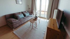 A living room with a sofa, a small table, a TV, and a window with curtains. - Vacation apartment "Ammersee" at Andechs Monastery (Andechs)