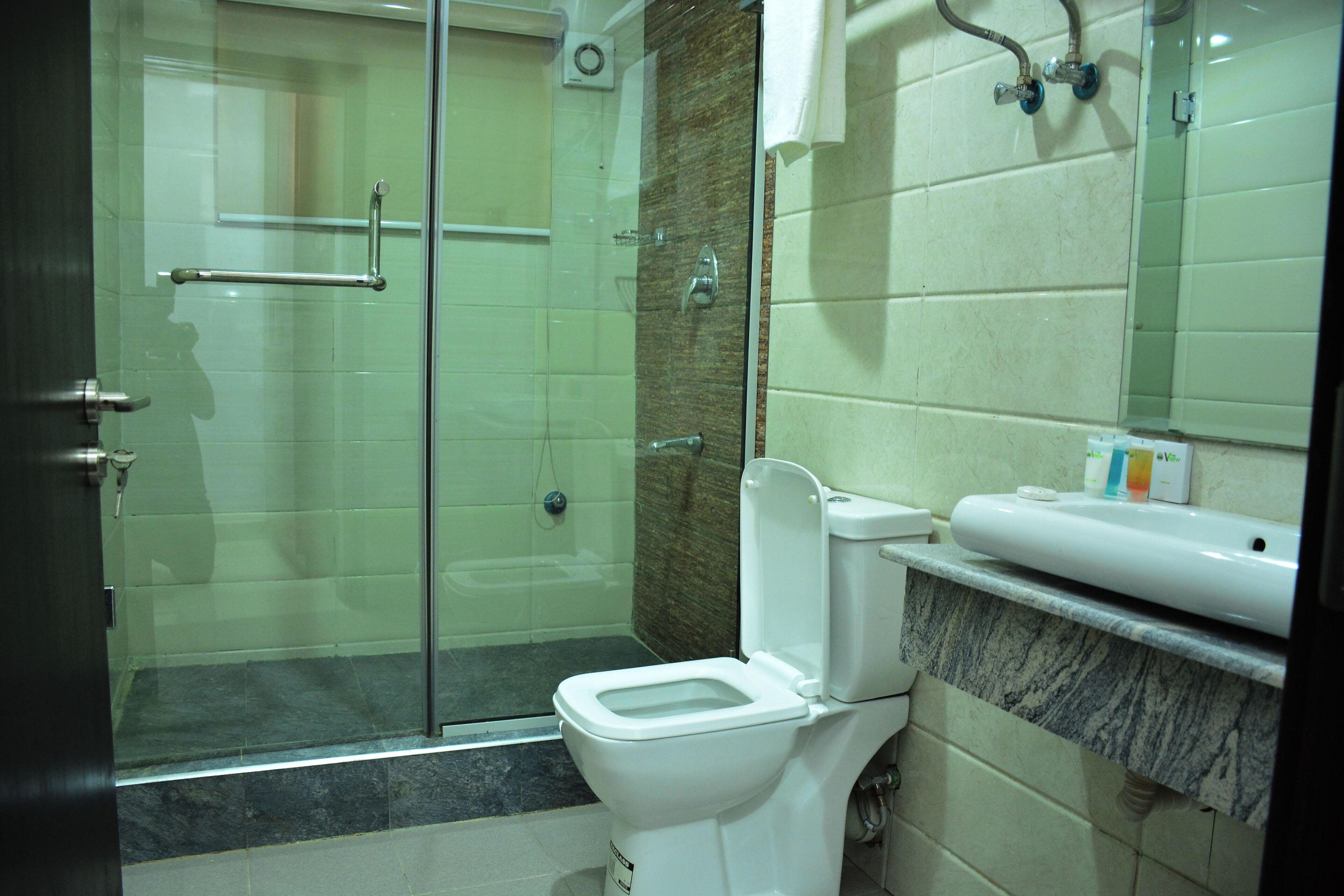 Une salle de bain avec une douche à parois de verre, des toilettes blanches et un plan de toilette en marbre avec un lavabo.