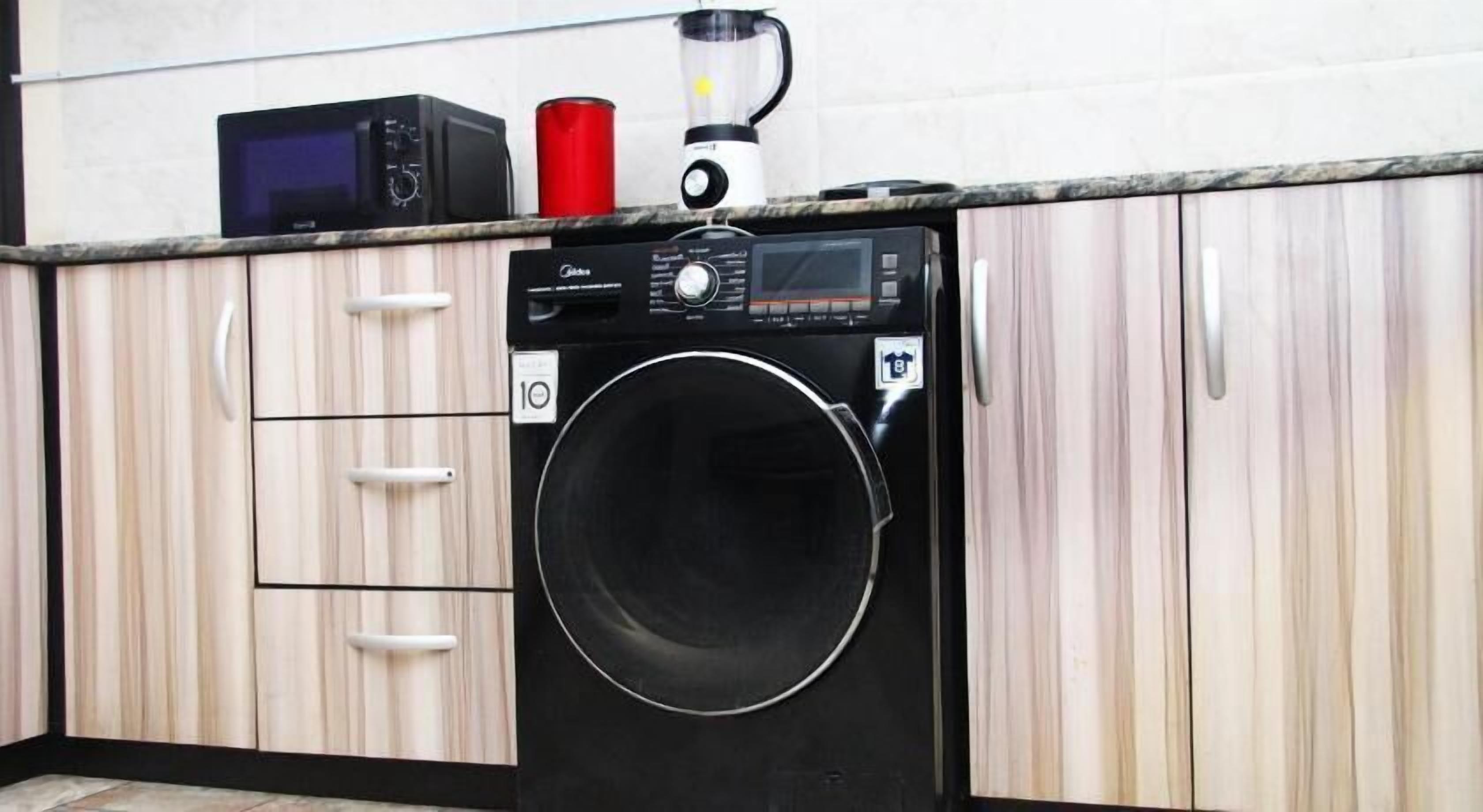 A compact kitchen with a washing machine, a microwave, and a blender on the countertop.