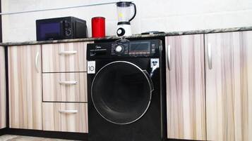 A compact kitchen with a washing machine, a microwave, and a blender on the countertop.