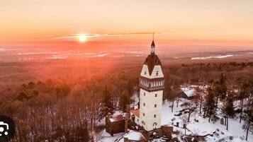 Una torre con aguja, rodeada de edificios y árboles cubiertos de nieve, durante el atardecer.