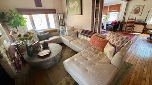 Un salon spacieux avec un grand canapé d’angle beige, une table basse ronde et une plante en pot.