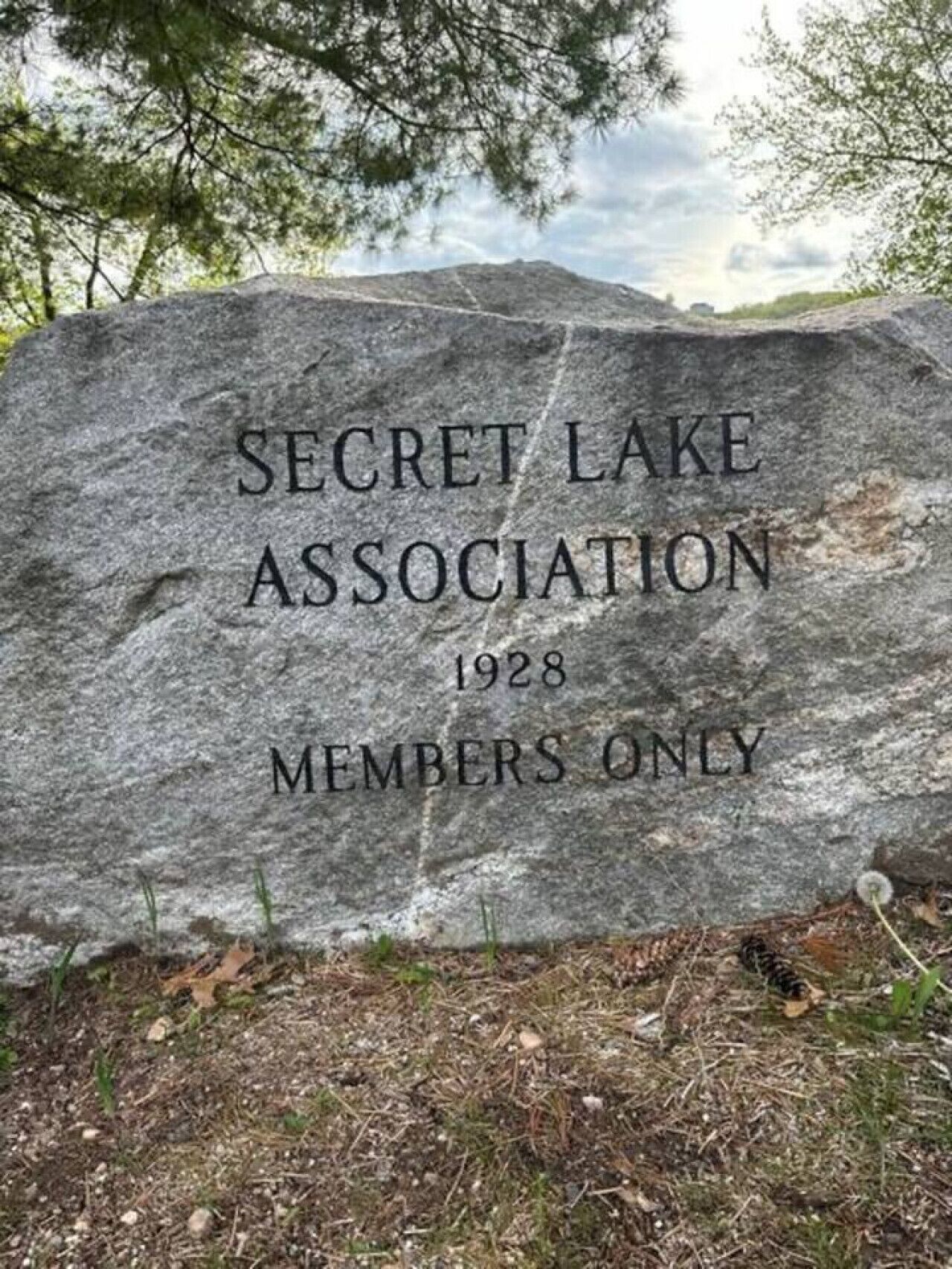 A large stone with the inscription "SECRET LAKE ASSOCIATION 1928 MEMBERS ONLY" surrounded by trees.