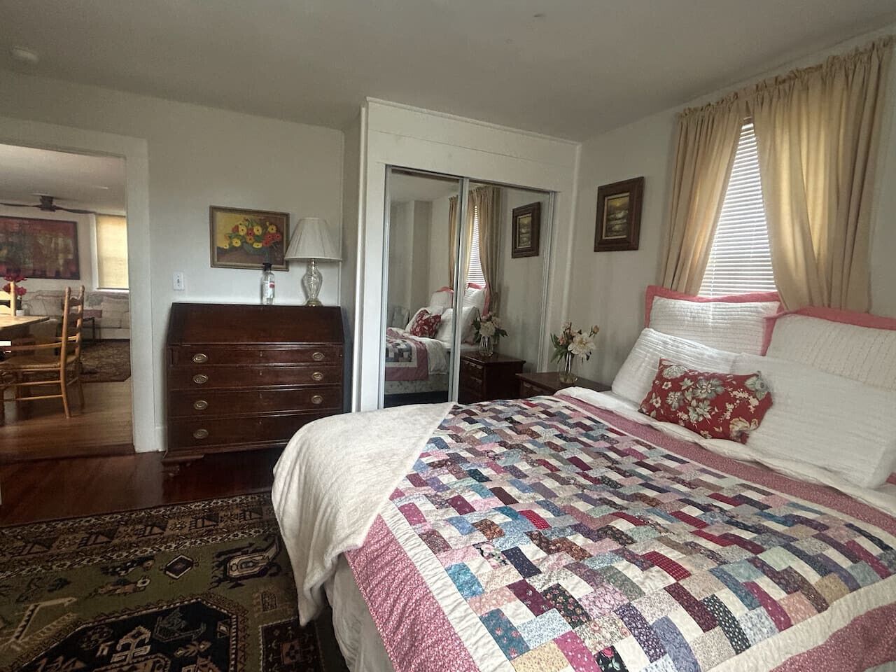 A bedroom with a large bed, a dresser, a mirror, and a door leading to another room.