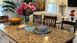 A kitchen with granite countertops, a dining area with a table and chairs, a ceiling fan, and a painting on the wall. - The Old Avon Village (Avon)