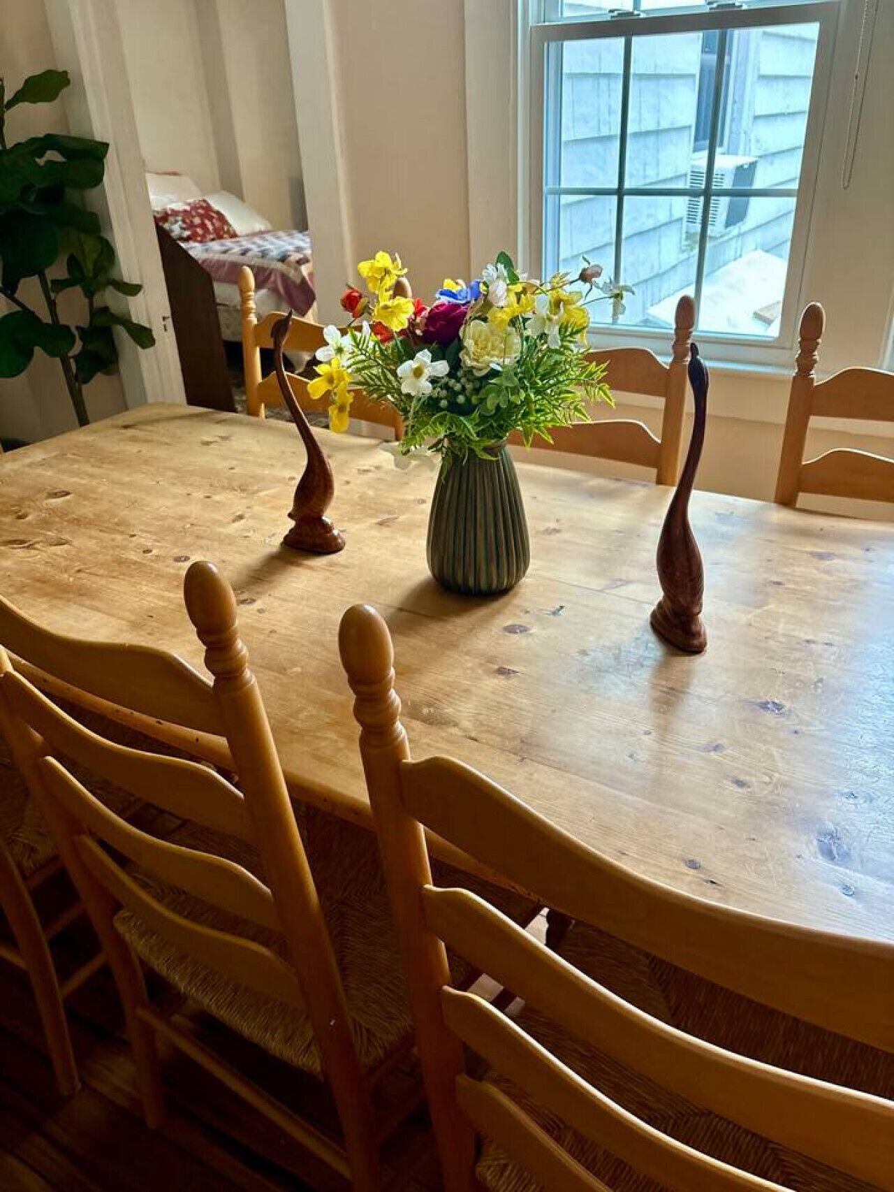 A wooden dining table with a vase of flowers in the center, surrounded by wooden chairs.