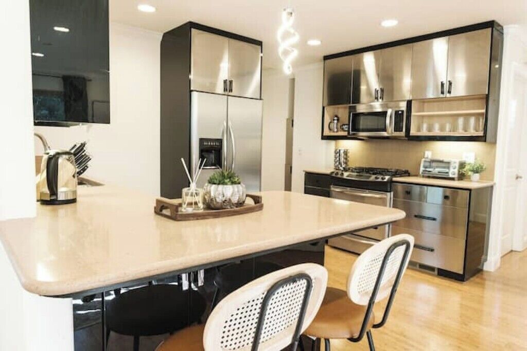 A modern kitchen with a central island, stainless steel appliances, and a seating area with two chairs.