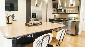 A modern kitchen with a central island, stainless steel appliances, and a seating area with two chairs. - Serene Escape 2BD /w Private Patio near Stanford (Menlo Park)