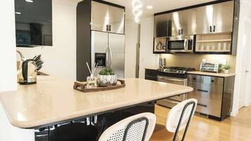 A modern kitchen with a central island, stainless steel appliances, and a seating area with two chairs.