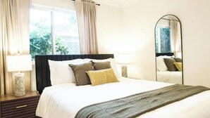 A hotel room with a bed, a nightstand, a lamp, a mirror, and a window with curtains. - Serene Escape 2BD /w Private Patio near Stanford (Menlo Park)