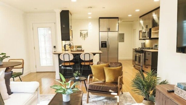 A modern living room with a sofa, coffee table, and chairs. There is a kitchen area with a refrigerator, microwave, and stove. - Serene Escape 2BD /w Private Patio near Stanford (Menlo Park)