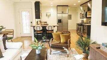 A modern living room with a sofa, coffee table, and chairs. There is a kitchen area with a refrigerator, microwave, and stove.