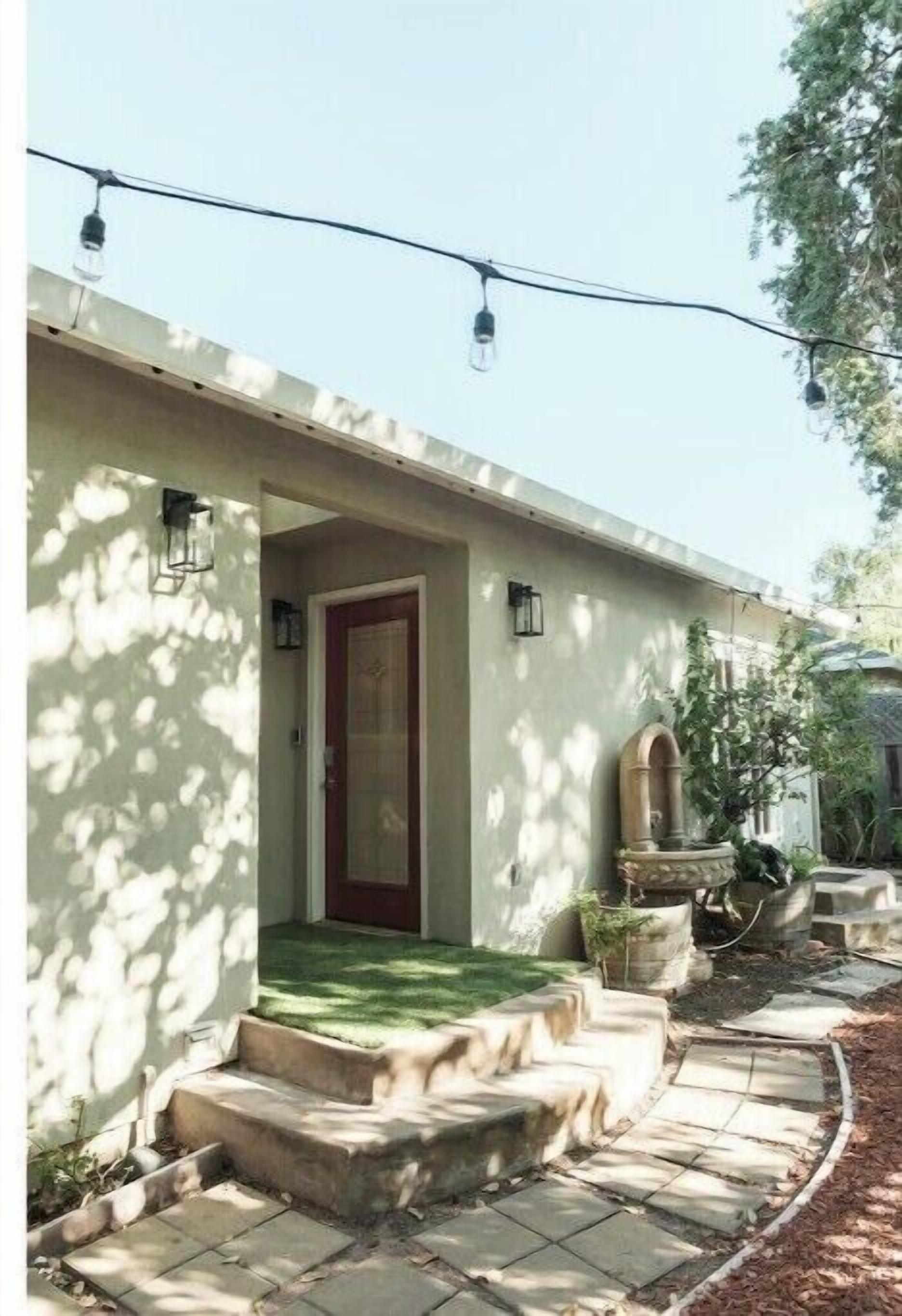 A house with a red door, a small porch, and a garden area with steps leading to the door.