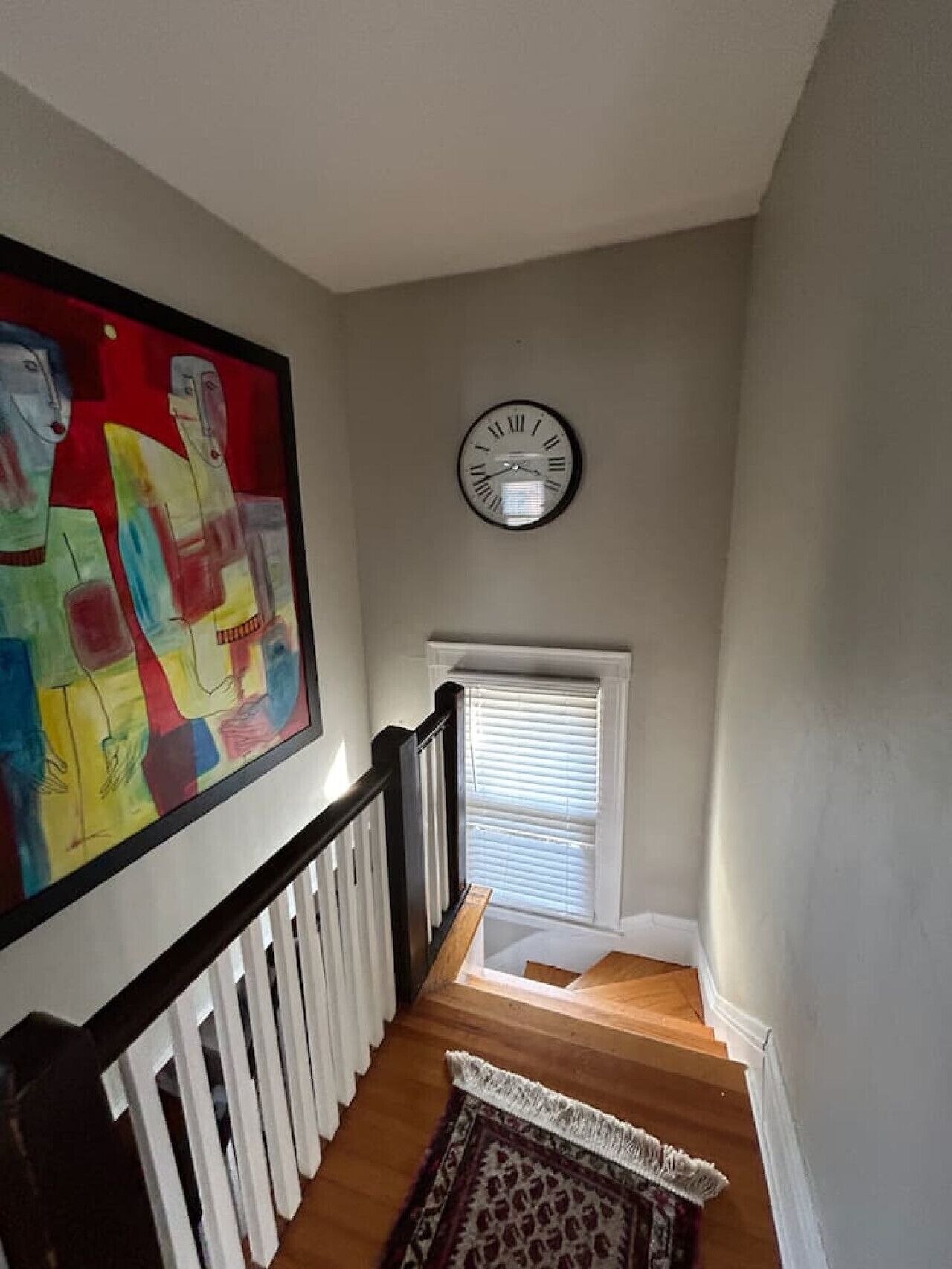 A staircase with a white railing, a clock on the wall, and a colorful abstract painting above it.