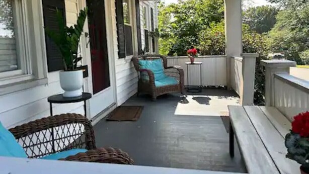 Een overdekte veranda met rieten meubels, een bloempot en een kleine tafel.