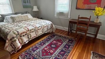 Une chambre à coucher avec un lit, un plancher en bois, un ventilateur de plafond, une chaise, un bureau et une fenêtre avec des stores.