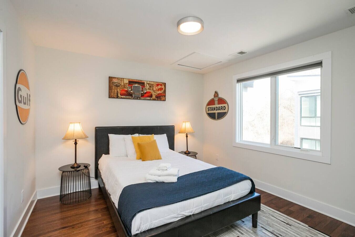 A neatly arranged bedroom with a bed, two bedside lamps, a painting, and a window.