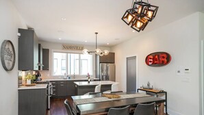 A modern kitchen with dark cabinets, a central island, and a dining area with a bar sign. - Luxury Escape | Spacious & Safe, 7min to Downtown! (Nashville)