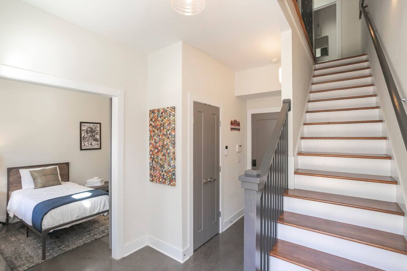 A hotel room with a bed, a nightstand, a wall art piece, and a staircase.