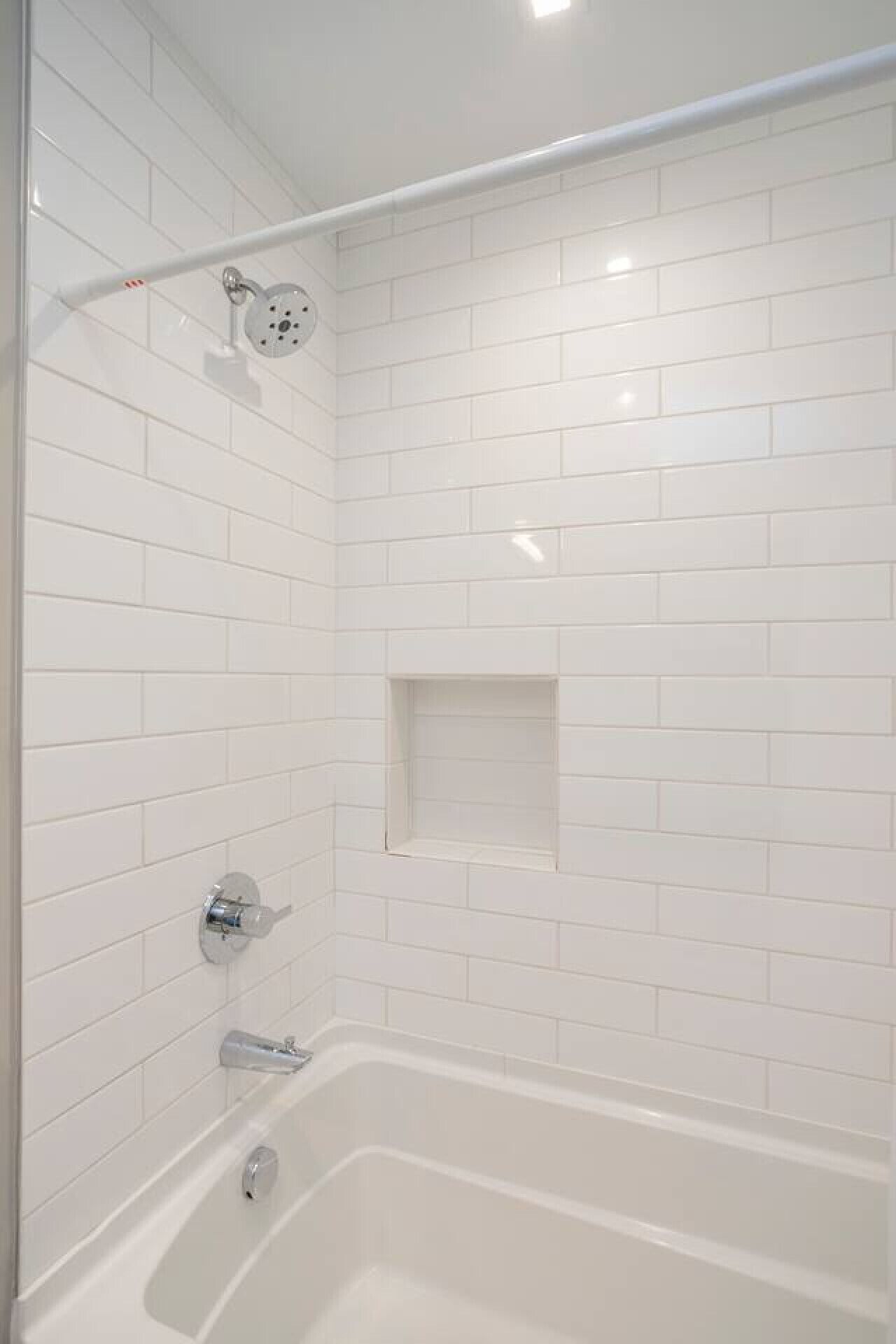 A modern bathroom with white subway tiles, a glass shower enclosure, a white bathtub, and a small shelf.