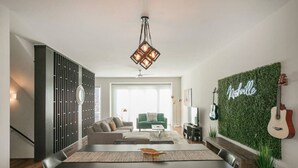A modern living room with a dining area, a staircase, and a wall with a guitar and a sign. - Luxury Escape | Spacious & Safe, 7min to Downtown! (Nashville)