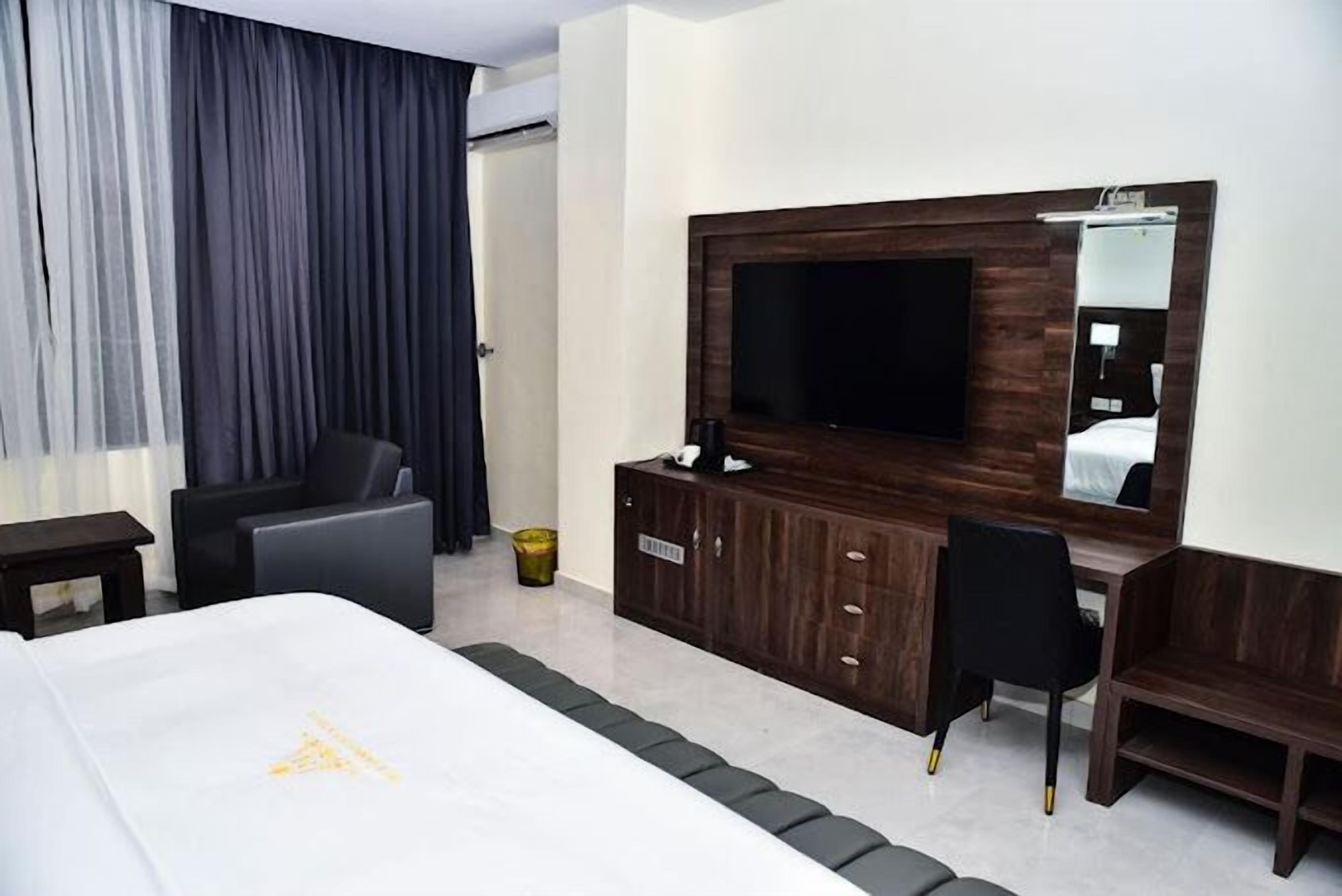 Una camera d'albergo con un letto grande, una scrivania con una sedia, una televisione e un armadio.
