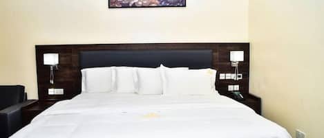 A hotel room with a large bed, two bedside tables with lamps, a wall-mounted air conditioner, and a floral artwork above the bed.