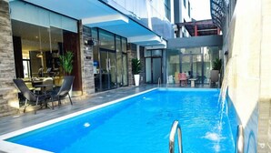 Una piscina interior moderna con agua azul cristalina, rodeada de paredes de vidrio y un muelle de madera.