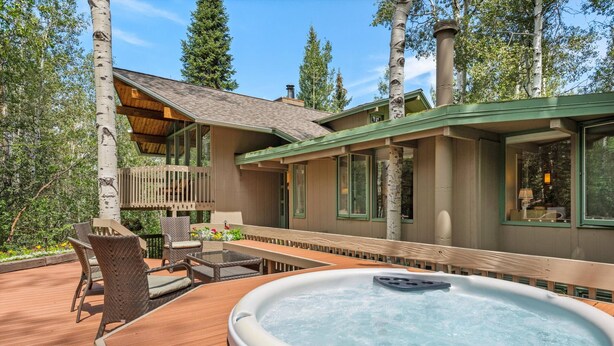 Un bain à remous sur une terrasse en bois, agrémentée de mobilier d’extérieur, le tout entouré d’une clôture en bois et de bouleaux.