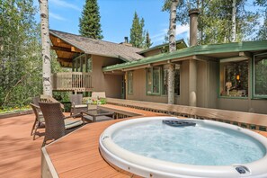 Een hottub op een houten terras met buitenmeubilair, omringd door een houten omheining en berkenbomen.