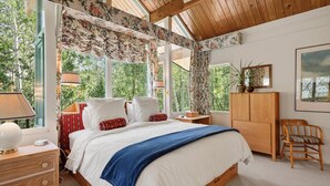 Une chambre à coucher avec un grand lit, une tête de lit en bois, une table de chevet, une commode, une chaise et une fenêtre avec des rideaux.