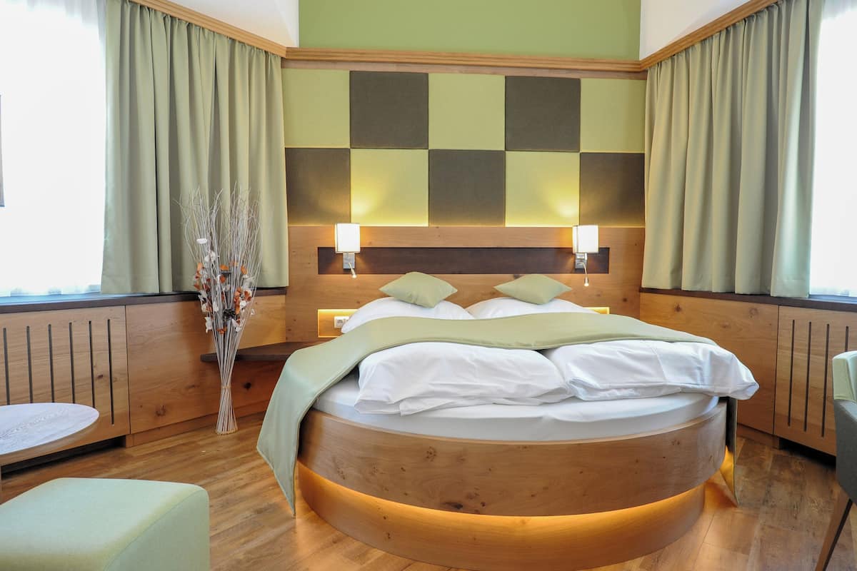 A circular bed with a wooden headboard, two bedside lamps, and a vase of dried flowers.