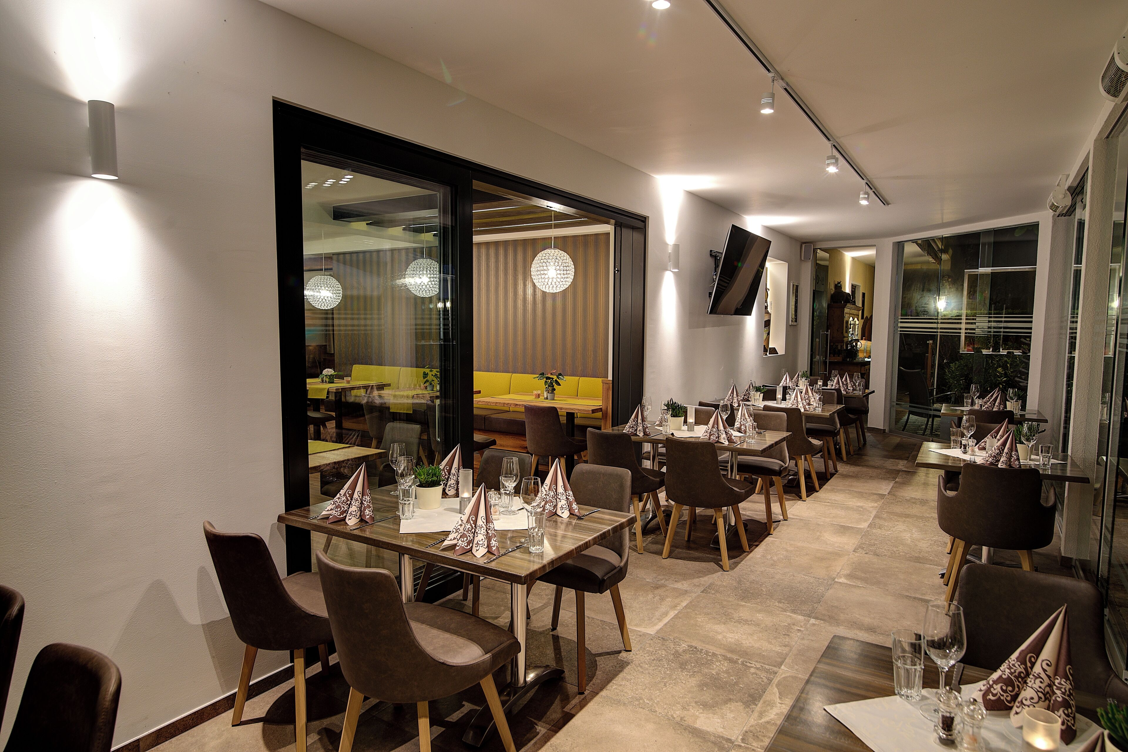 Un restaurant moderne doté de plusieurs tables et chaises, d’une grande fenêtre et d’un téléviseur à écran plat fixé au mur.