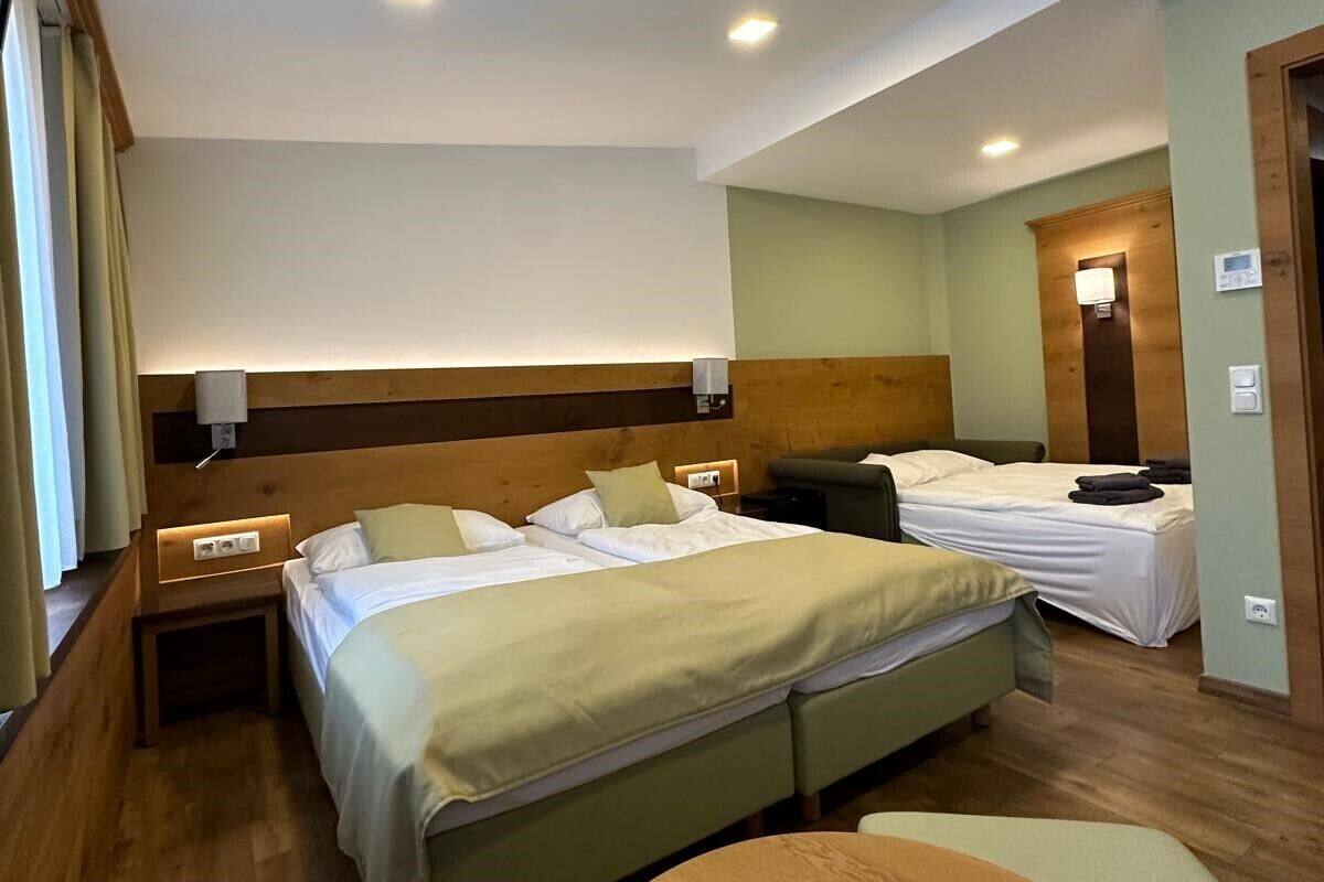 A hotel room with a large bed, a smaller bed, a wooden table, and a nightstand with a lamp.